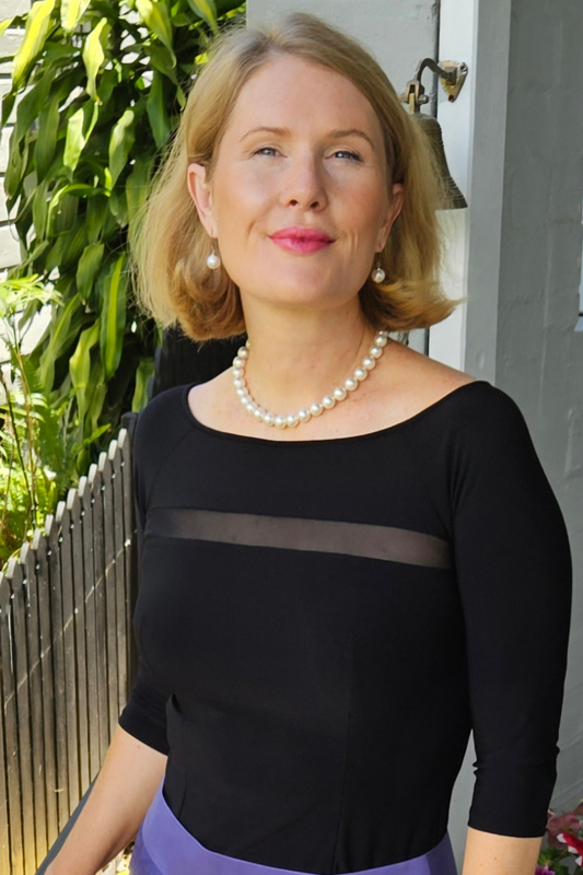 Woman wearing a black top with sheer panels and a pearl necklace outdoors.
