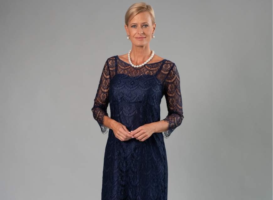 Woman wearing a navy lace dress against a gray background